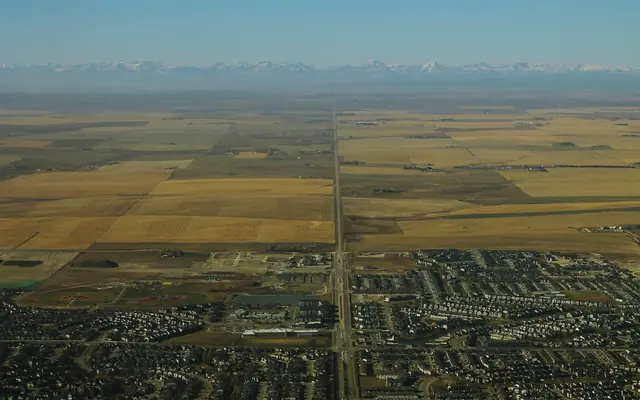 Aerial view west over Airdrie's neighbourhoods and farmland toward the Rocky Mountains