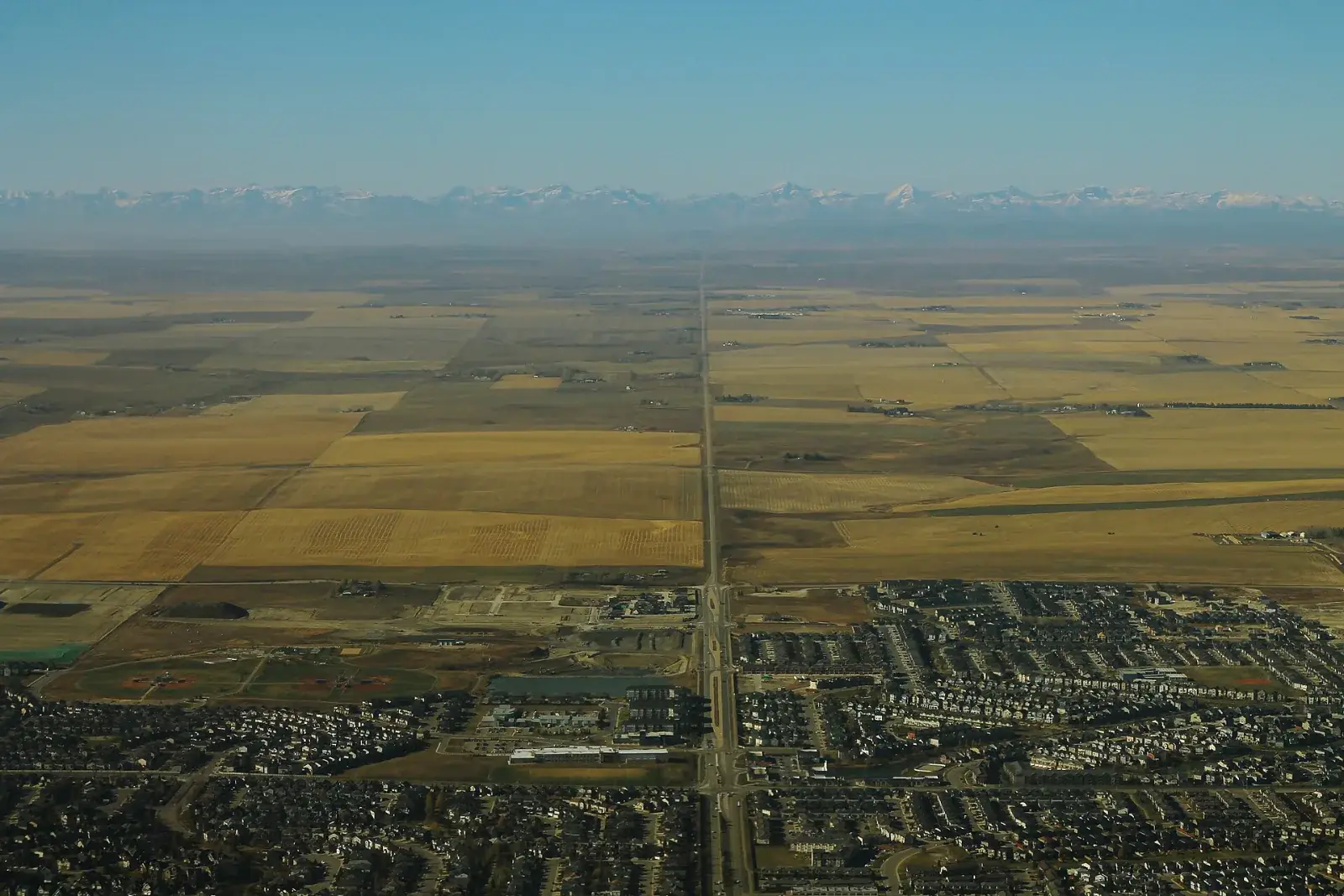 Aerial view west over Airdrie's neighbourhoods and farmland toward the Rocky Mountains